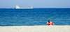 La Pineda, Vila-seca, Costa Dorada, Tarragona, Catalonia: woman on a deck chair and a passing freighter - photo by B.Henry