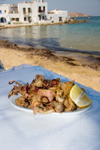 Greece - Paros: Calimari on table in foreground with background Naousa beach and village - photo by D.Smith